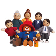 A set of wooden family and pet doll figures with fabric clothing and accessories, including a central figure in a red hat and coat, surrounded by six other wooden characters on a plain white background.