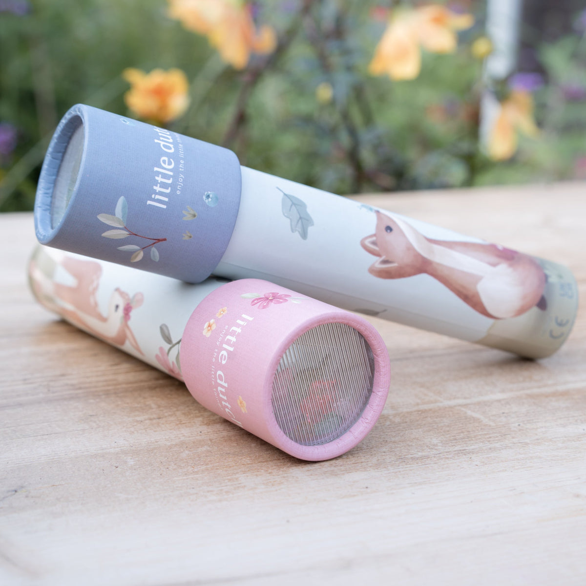 Two cylindrical speakers, one pink and one purple, with floral designs on a wooden surface.