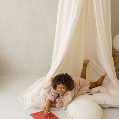 Child playing with a red book under a canopy in a cosy room.
