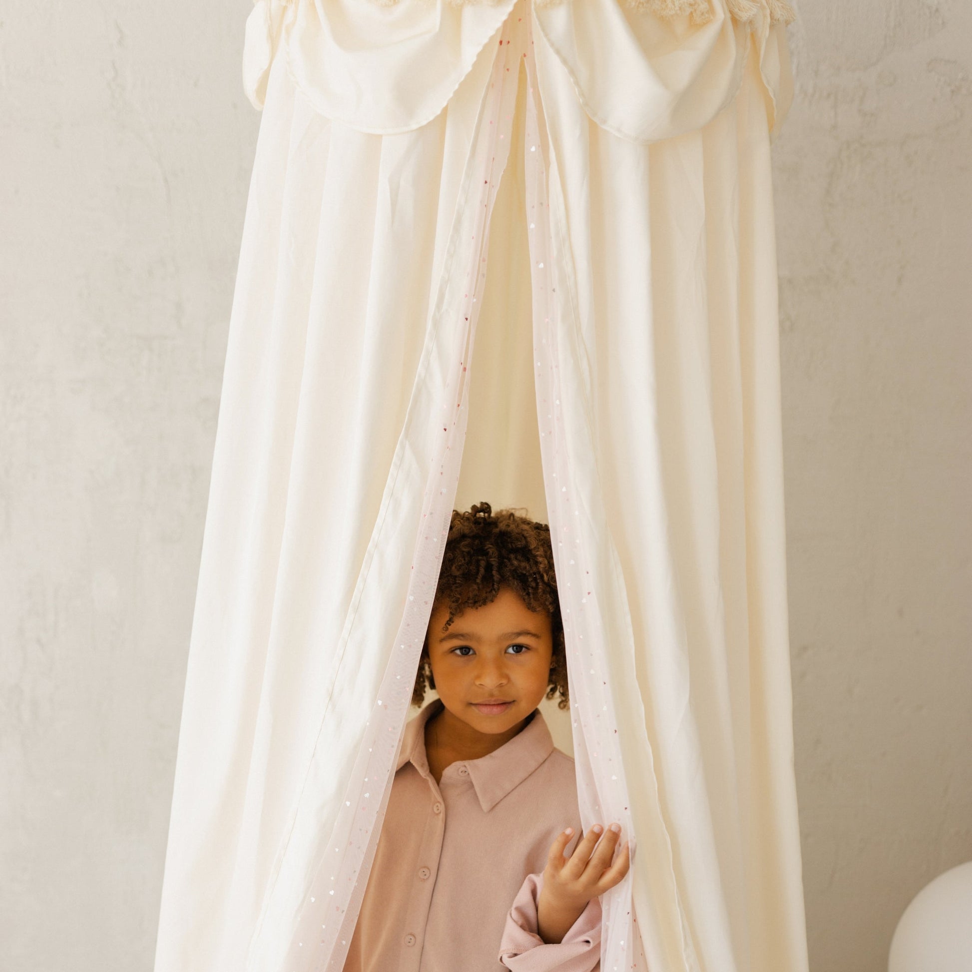 Child peeking through a white canopy in a softly lit room