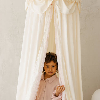 Child peeking through a white canopy in a softly lit room
