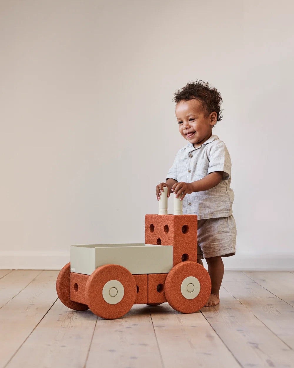 Child playing with a wooden toy car on a wooden floor.