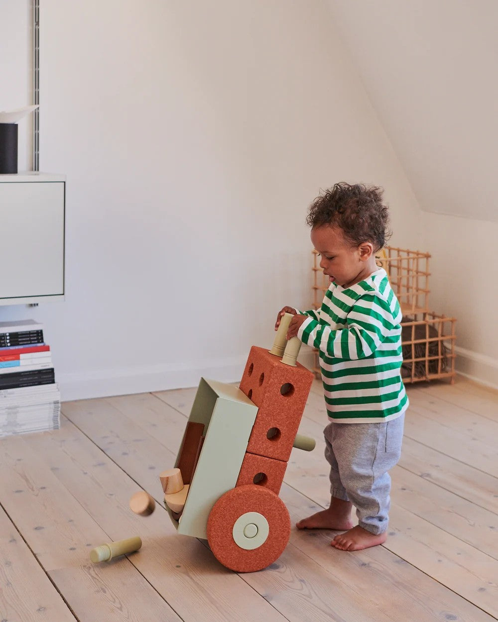 Child playing with a wooden toy in a room with a white wall and wooden floor.