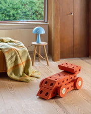 Red geometric toy on a wooden floor with a blue lamp and window in the background
