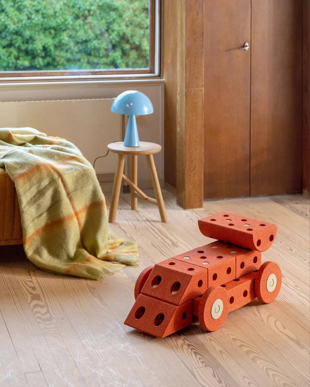 Red geometric toy on a wooden floor with a blue lamp and window in the background