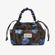 A Tiba + Marl handbag with a brown base and blue floral print, featuring a gathered top handle and a front patch logo.