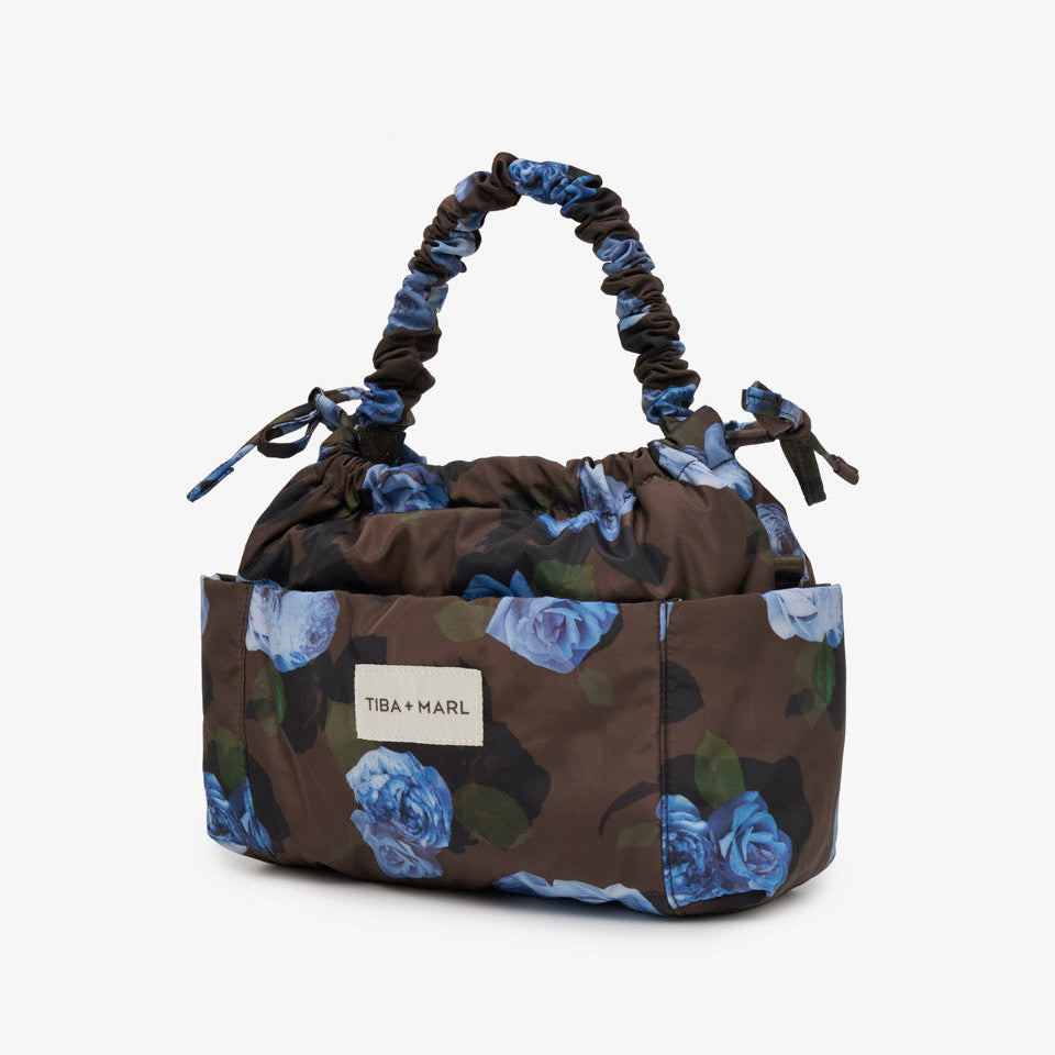 A Tiba + Marl handbag with a dark brown base, blue and white floral print, and a distinctive gathered top handle, shown on a light gray background.
