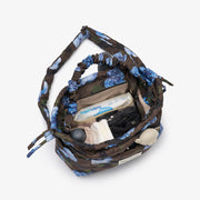 A top-down view of a drawstring bag with a blue and brown camouflage floral pattern, shown open with its contents visible, including a water bottle and toiletries, on a light gray background.