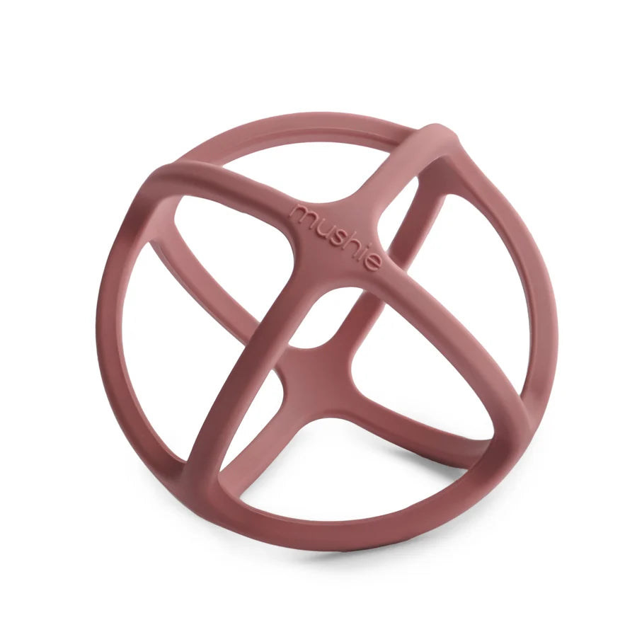 A Mushie dusty rose silicone teether in a spherical shape, open-frame design and the brand name 'mushie' embossed on the center, shown on a clean white background.