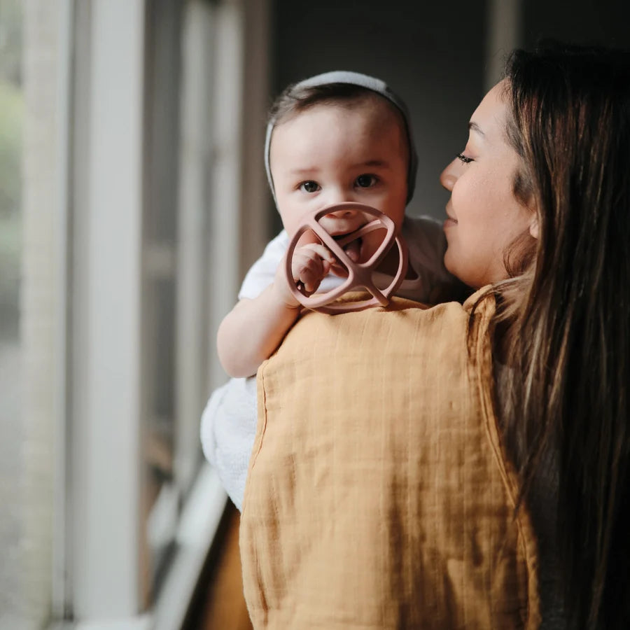 Woman holding a baby with a mushie teether standing indoors.
