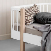 Oliver Furniture Wood Original Junior Day Bed in white and oak with pillows and a gray blanket on a gray painted floor. 