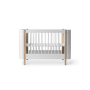 Oliver Furniture Wood Mini+ Cot Bed with Junior Kit in white and oak, a convertible 0-9 years sleeping solution featuring adjustable cot base, removable bars, and junior bed conversion capability.