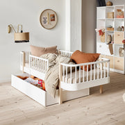 Modern Scandinavian nursery bedroom featuring Oliver Furniture Wood Original white and natural birch bed with integrated safety guard rail, matching storage shelving, and neutral bedding in a minimalist interior design.