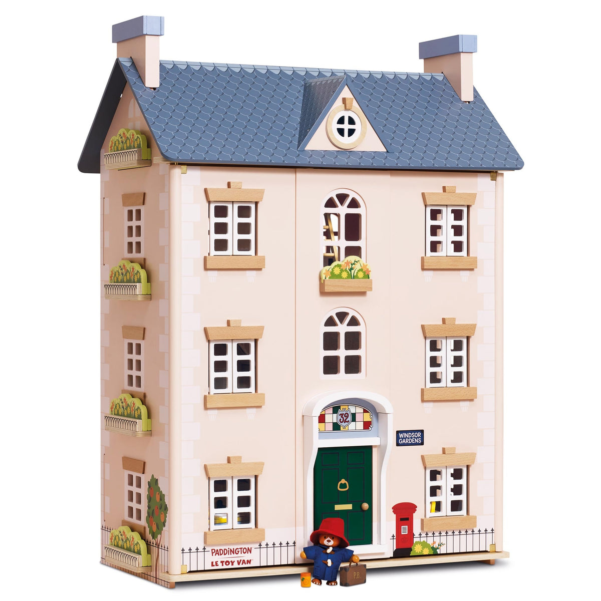 A wooden le toy van dolls house of Paddington's house in London, featuring a beige facade, blue-gray tiled roof, green front door, red postman hat, and a small Paddington Bear figure standing in front.