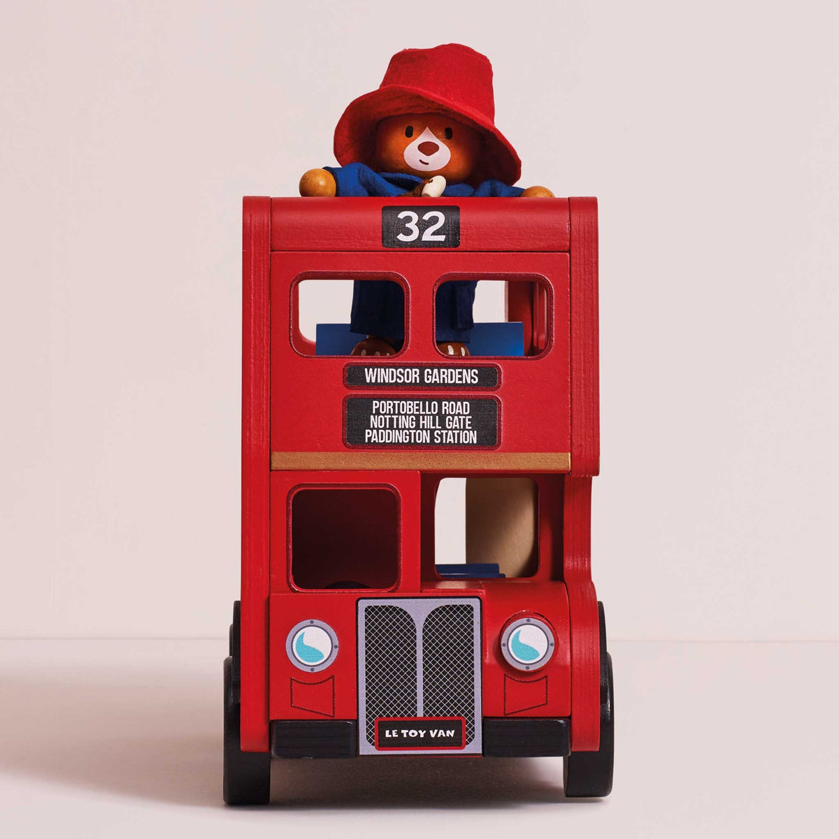 A red double-decker toy bus with a Paddington Bear figure sitting on top, photographed against a plain light beige studio background.