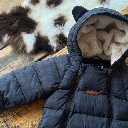 A navy blue puffer jacket with a subtle houndstooth pattern, featuring a plush cream fleece lining inside the hood with cat ears, laid flat on a rustic wooden surface.