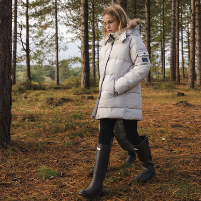 Girl walking through a forest wearing a long off white parka coat with the fur trim hood.