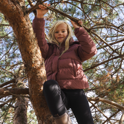 Girl climbing a tree wearing a dusty rose pink puffer jacket.