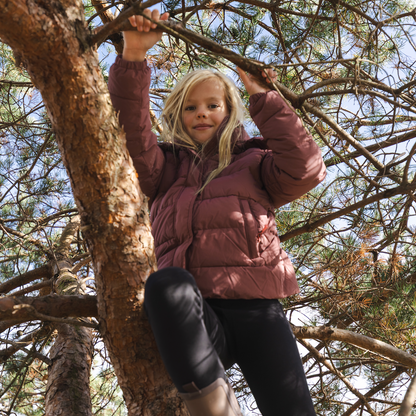 Girl climbing a tree wearing a dusty rose pink puffer jacket.