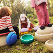 Children playing with colourful Stapelstein Stepping Stones in a mossy outdoor forest setting. 