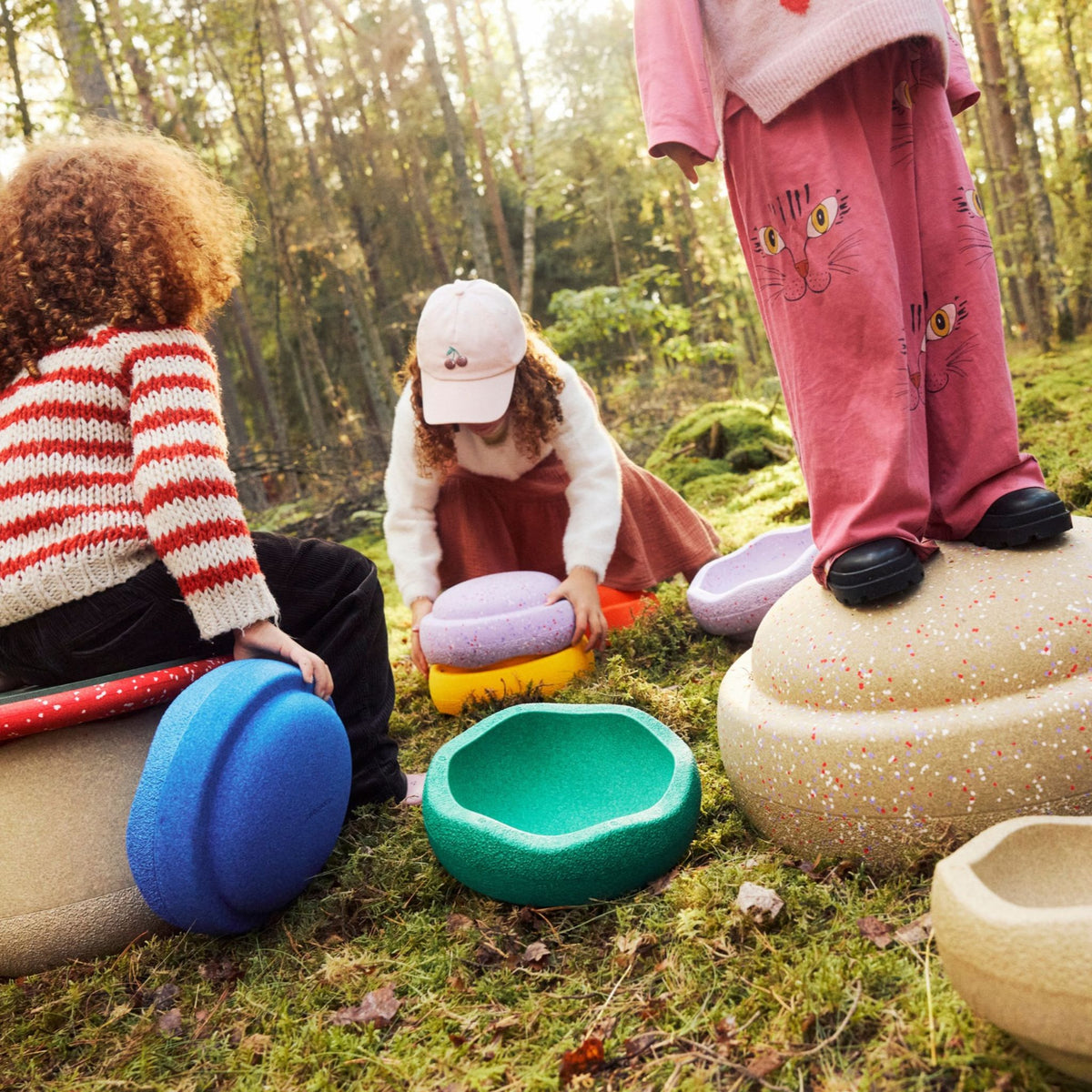 Children playing with colourful Stapelstein Stepping Stones in a mossy outdoor forest setting. 