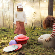 A child stands in a sunlit forest while another child sits beside playing with Stapelstein Winter Special Stepping Stones and Wobble Boards.