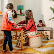 Lifestyle image of child's playroom scene with two children interacting at a small wooden table. One child stands while the other sits on a Winter Special Stapelstein Special Dynamic Set.