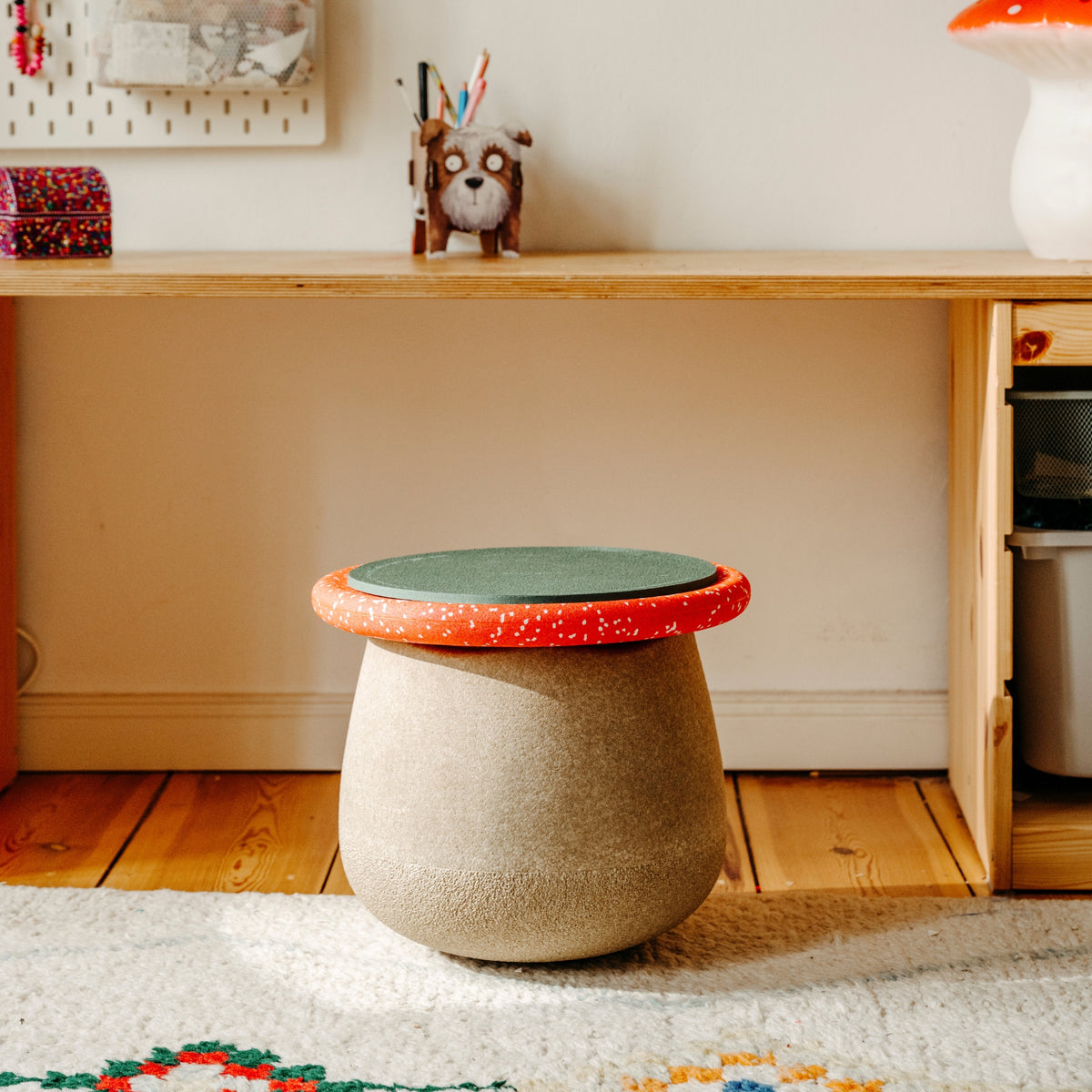 A small round Stapelstein Synamic Set stool with a textured beige body and a lid featuring a wobble board and green pad top.