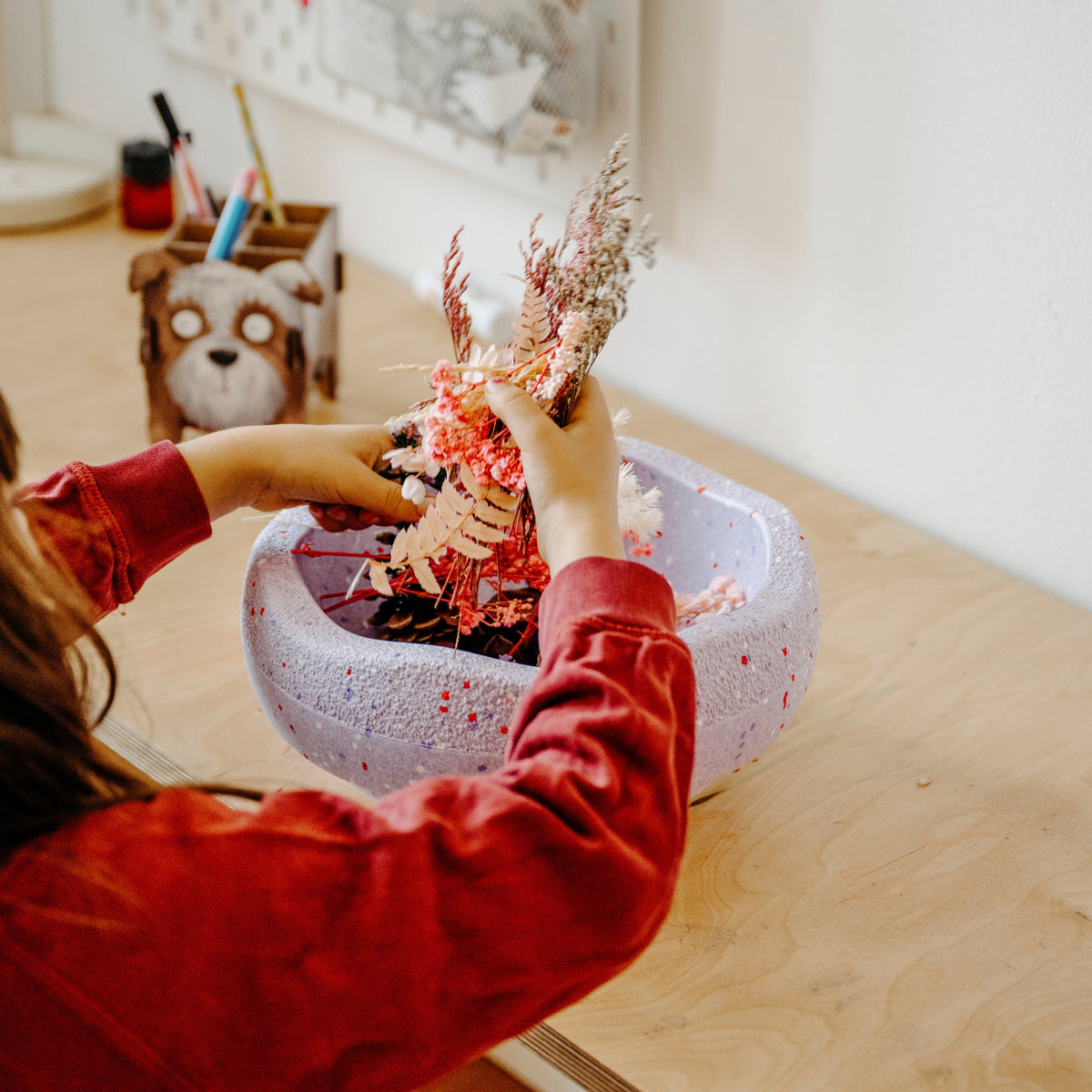 A person in a red long-sleeve top arranges a decorative dried floral arrangement in a speckled violet Stapelstein Stepping Stone.