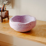 Stapelstein Winter Special lavender purple with red and purple speckles sits on a light wood desk in a warm indoor setting.