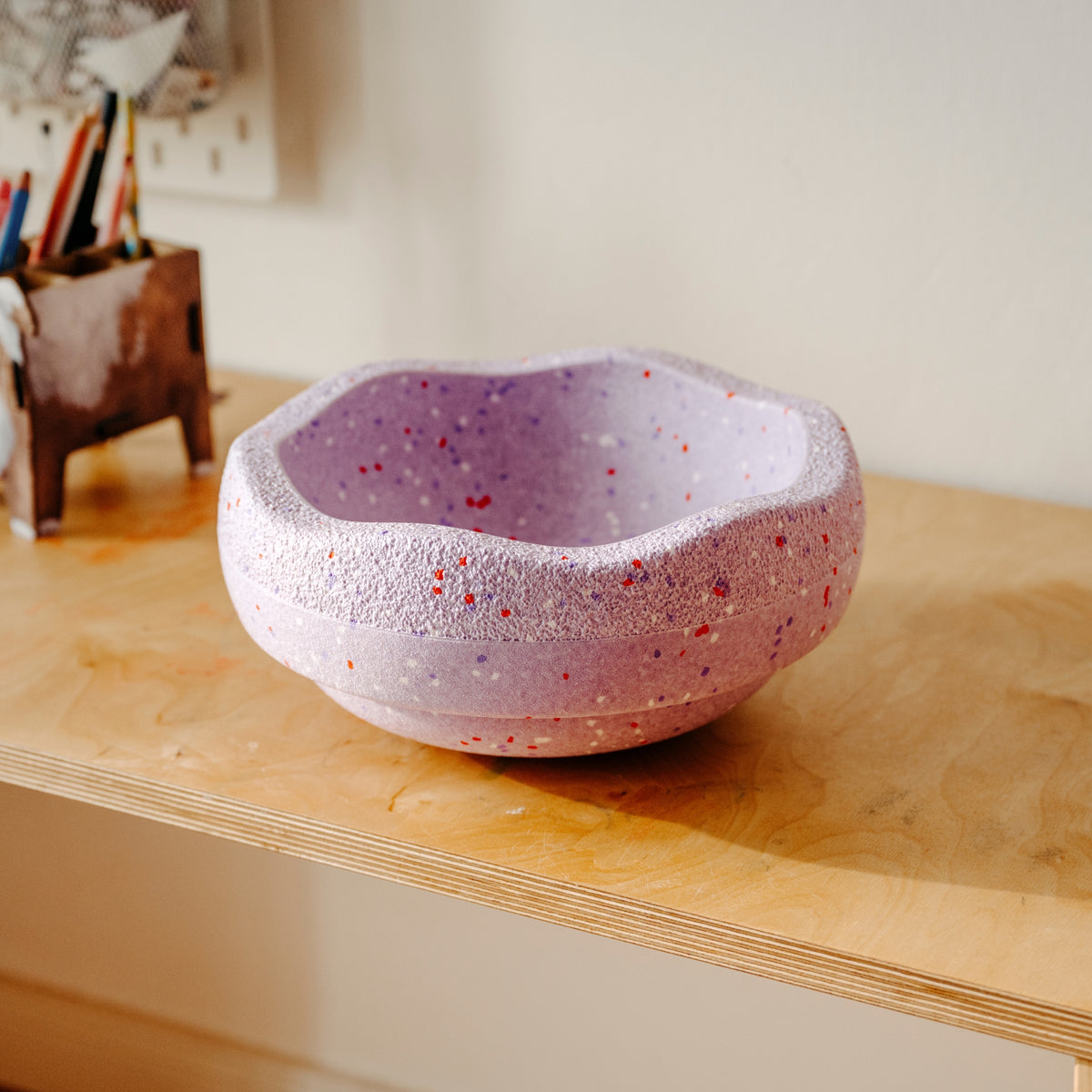 Stapelstein Winter Special lavender purple with red and purple speckles sits on a light wood desk in a warm indoor setting.