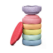 A set of six pastel-coloured, textured stapelstein stepping stones stacked vertically with one purple speckled stone resting on top, alongside a matching red wobble board.