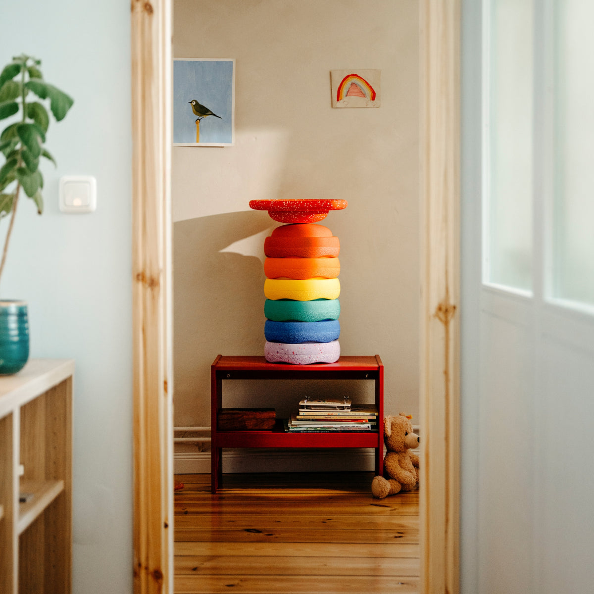 A colourful children's stacking toy of stapelstein stepping stones in red, orange, yellow, green, blue, purple, and a red wobble board.