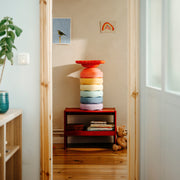 A colourful stacked ring-shaped toy set in shades of red, orange, yellow, green, blue, and pink, displayed on a small red side table in a child's room.