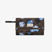 A Tiba + Harel zip-around wallet in a dark brown camouflage pattern with blue and white floral prints, featuring a white brand label on the front flap.