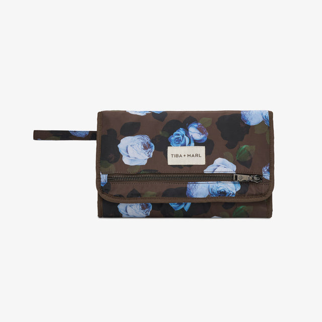 A Tiba + Harel zip-around wallet in a dark brown camouflage pattern with blue and white floral prints, featuring a white brand label on the front flap.