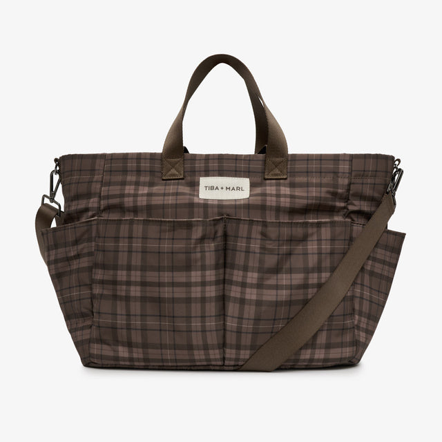 A brown and beige plaid diaper bag by TBA x Karl, featuring dual top handles, a detachable shoulder strap, and a white brand label on the front.