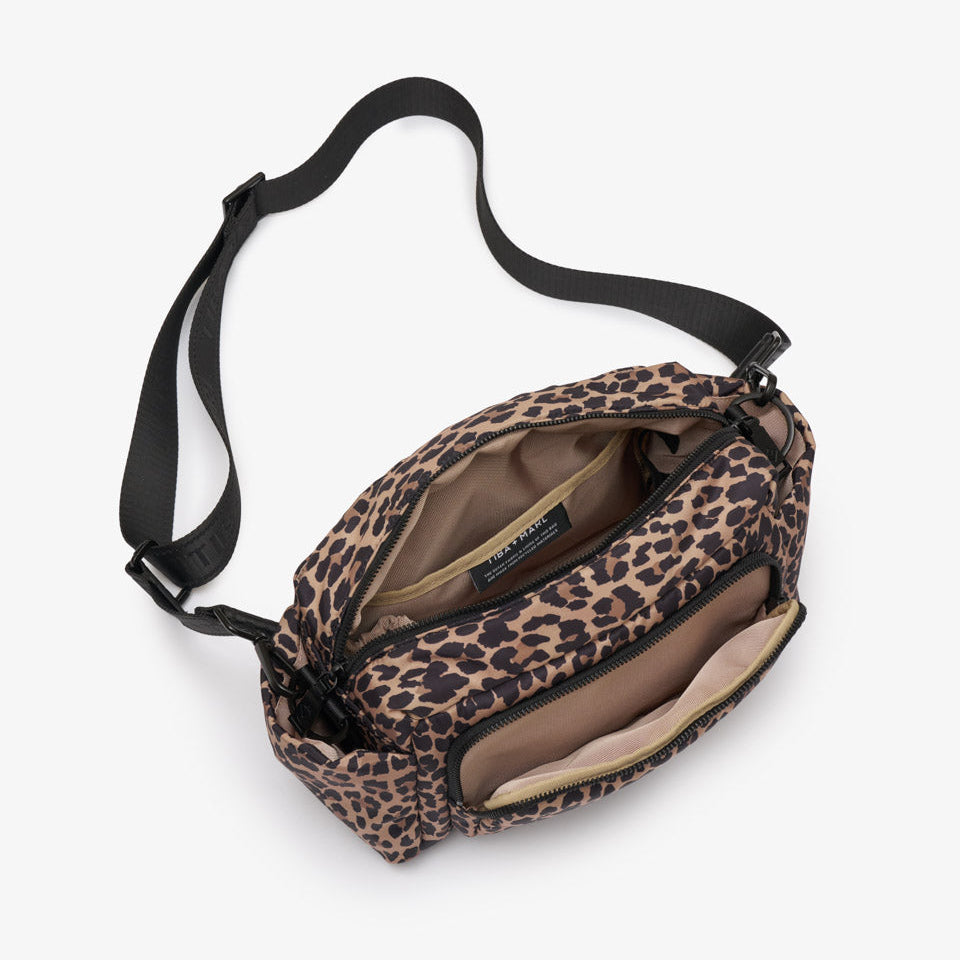 A leopard print crossbody bag with a black adjustable strap, shown open to reveal its interior compartments and a beige interior lining, photographed on a light gray background.