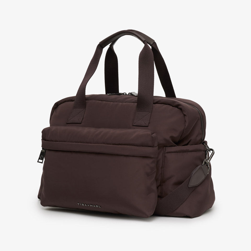 A dark brown nylon duffel bag with dual top handles, a front zippered pocket, and a side strap attachment, shown on a light gray background.