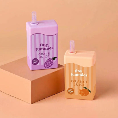 Two miniature juice carton-shaped drink straws by tiny tummies, one purple grape juice and one orange juice, displayed on a beige background with a brown block.