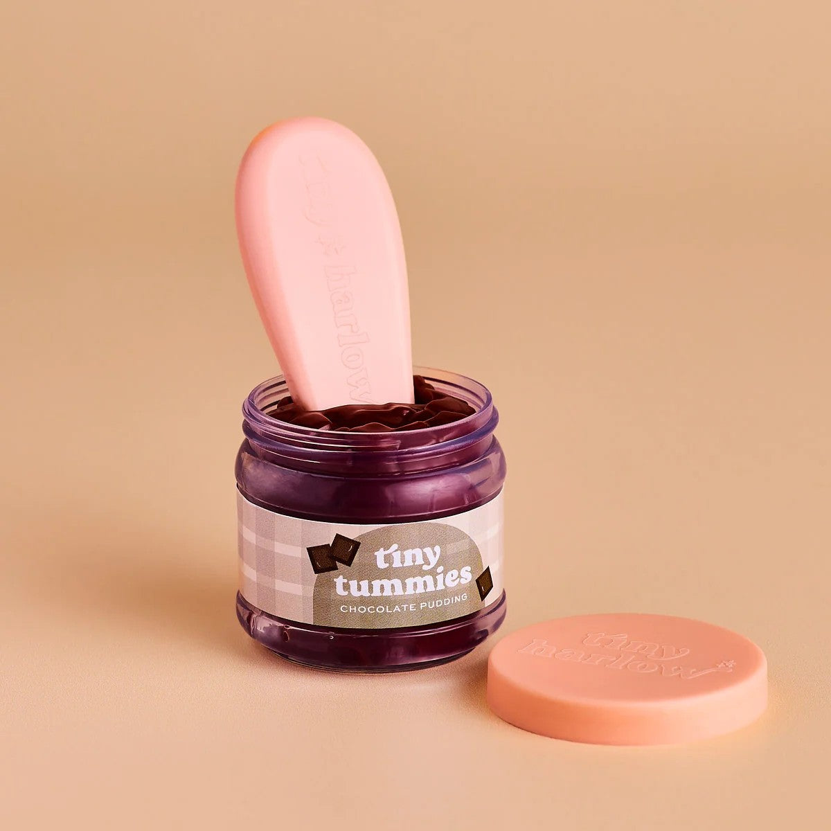 Jar of 'tiny tummies' chocolate pudding with a pink spoon on a beige background