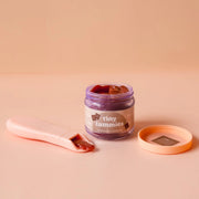 Jar of 'tiny tummies' chocolate pudding with a pink spoon on a beige background