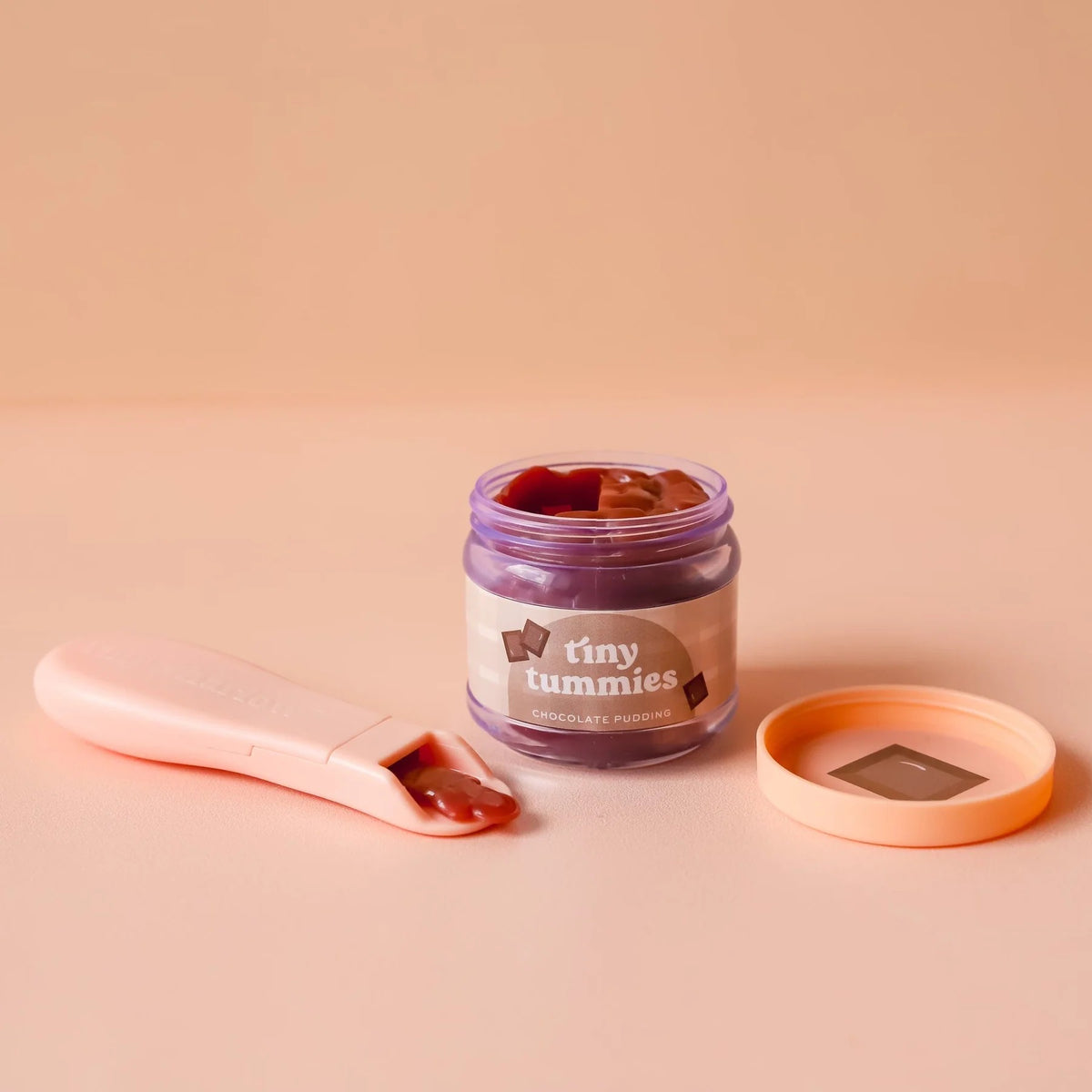 Jar of 'tiny tummies' chocolate pudding with a pink spoon on a beige background