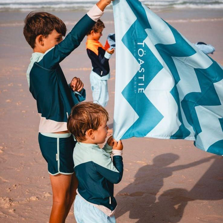 Two children holding a Toastie branded towel on a beach.