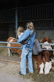 Person with a leopard print bag interacting with cows in a barn setting