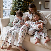 A family of four wearing matching Christmas pyjamas sits together on a cream-colored sofa in a cosy living room with a decorated Christmas tree in the background.