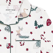 A close-up of a white long-sleeve pyjama top with a Christmas print, featuring green piping, a chest pocket, and motifs of reindeer, candy canes, mistletoe, and red stars. The brand name 'AVERY ROW' is visible on the inner neck label.