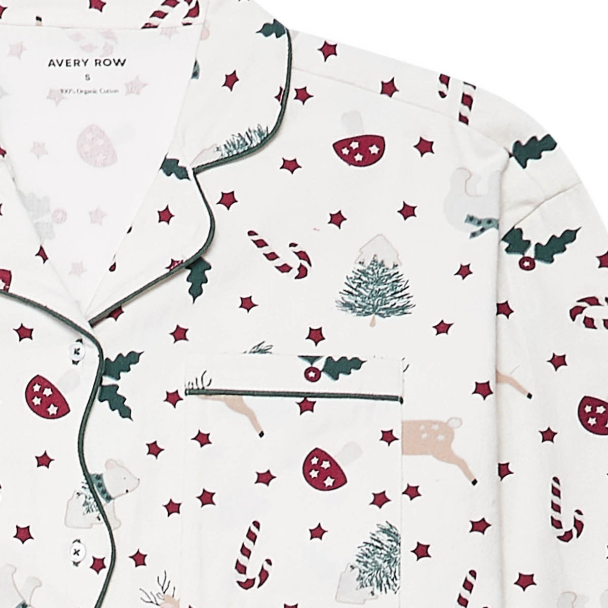 A close-up of a pyjama top with a festive Christmas print on an off-white background. The pattern features dark green holly leaves, red candy canes, red stars, beige reindeer, and green Christmas trees.