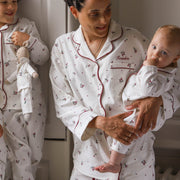 A woman and a baby wearing matching Christmas pyjamas with a holly leaves and berries print. The pyjama set has red piping.