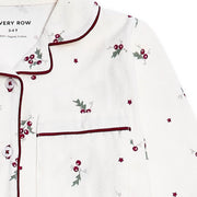 White long-sleeve pyjama top with dark red piping, featuring a chest pocket and an all-over holly and berry print with small star accents.